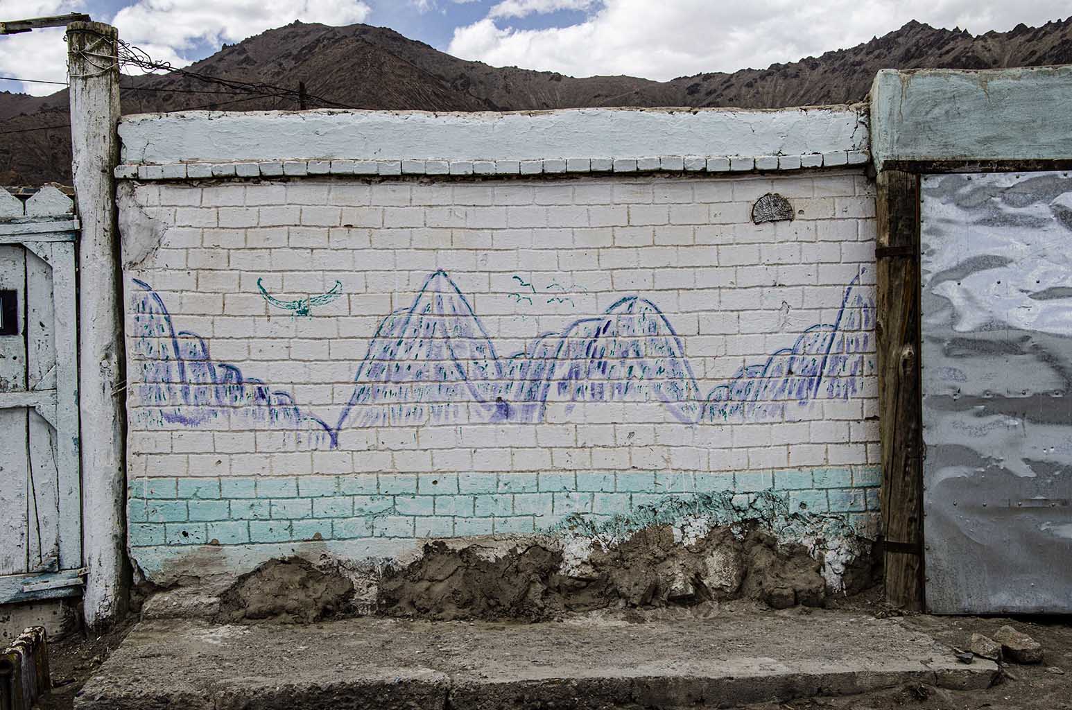 Photo of an outdoor wall mural in Murghab, Gorno-Badakhshan Autonomous Region, Tajikistan, featuring a scene of mountains and sky.